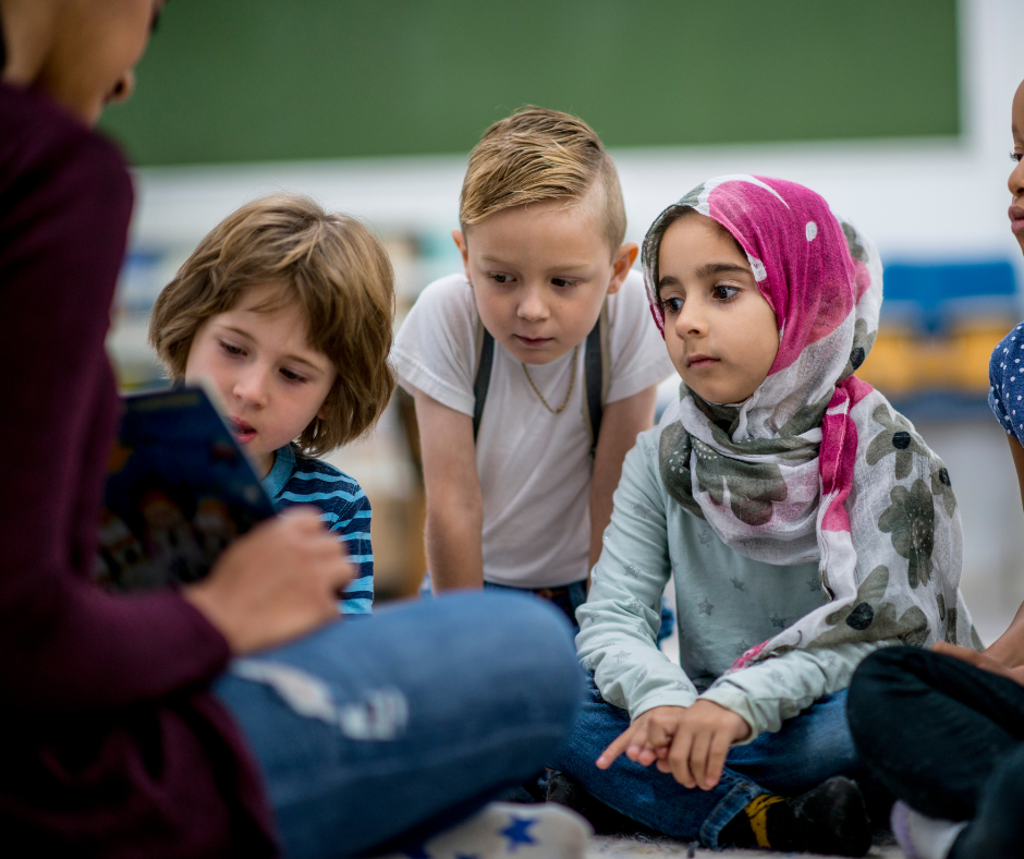 a group of children seated around an adult who is showing them a book